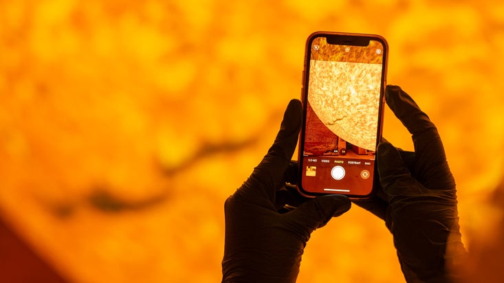 An image of Helios the sculpture of the sun on a phone screen with sculpture out of focus in the background